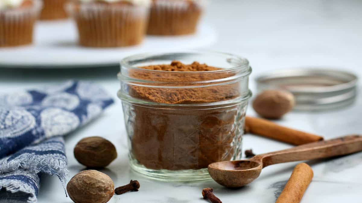 Pumpkin spice in a jar with a spoon and cinnamon sticks.