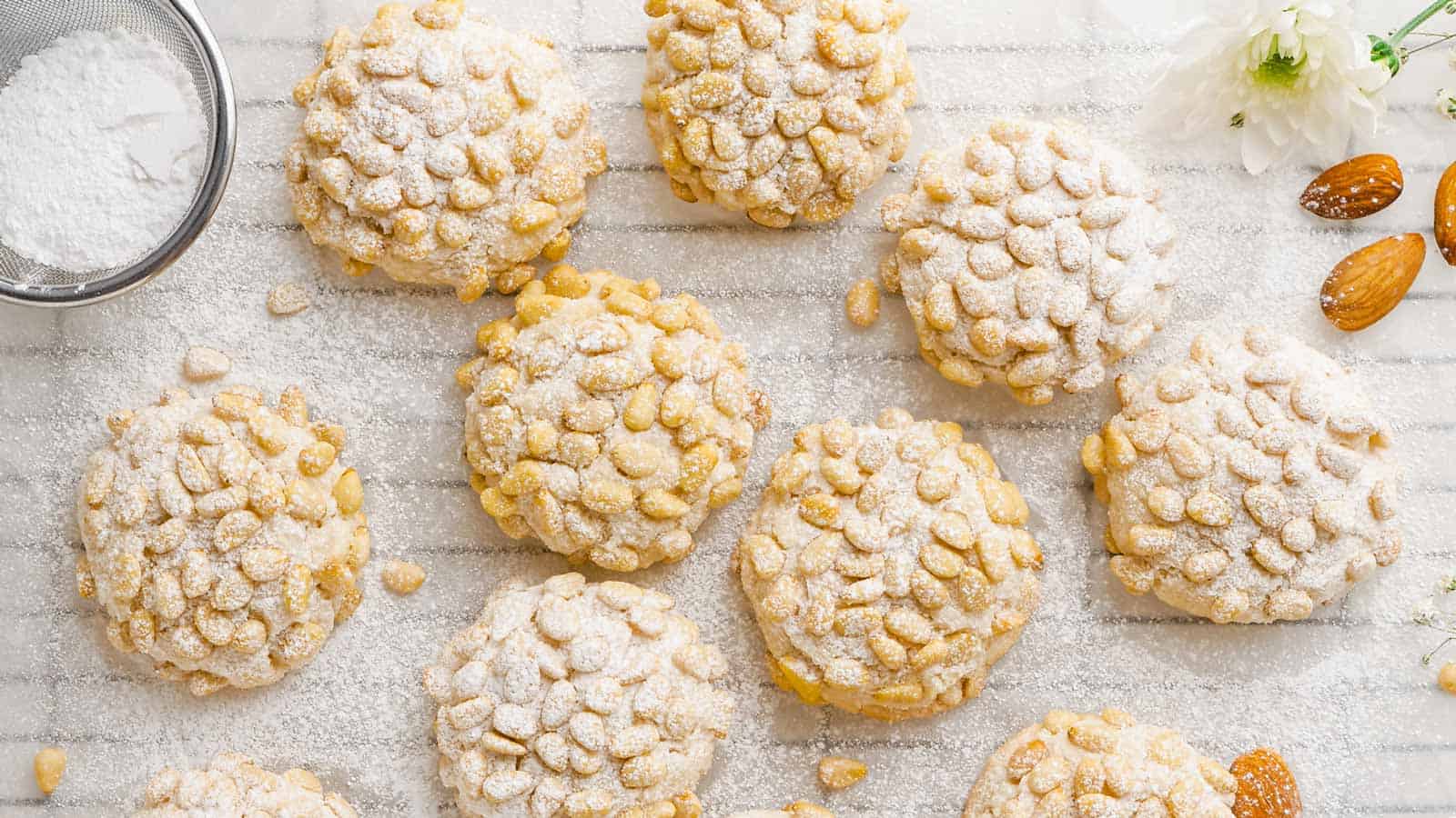 Pignoli cookies covered in powdered sugar on a white piece of parchment paper.