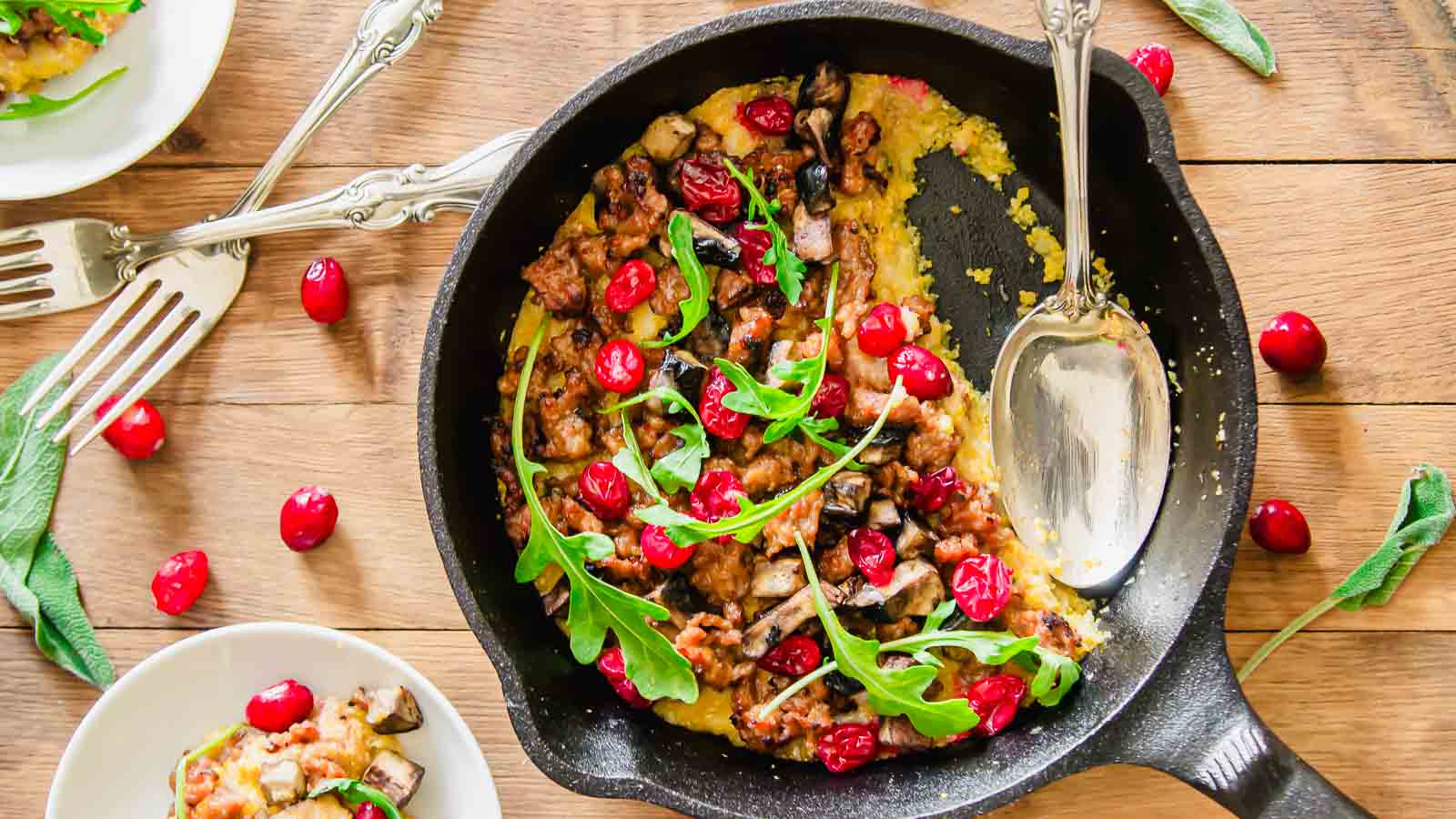 A serving spoon in a cast iron skillet with polenta and sausage.