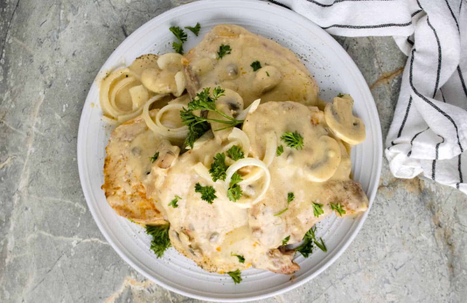 Pork chop topped with onion gravy on a white plate.