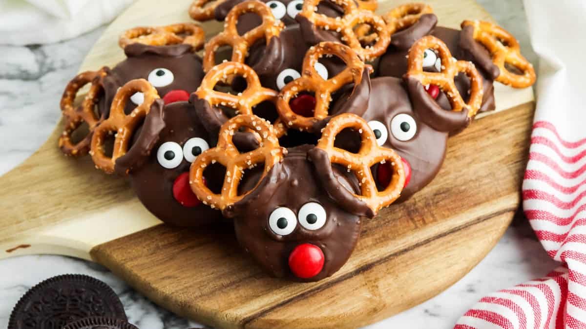 Reindeer cookie with pretzel antlers on a cutting board.