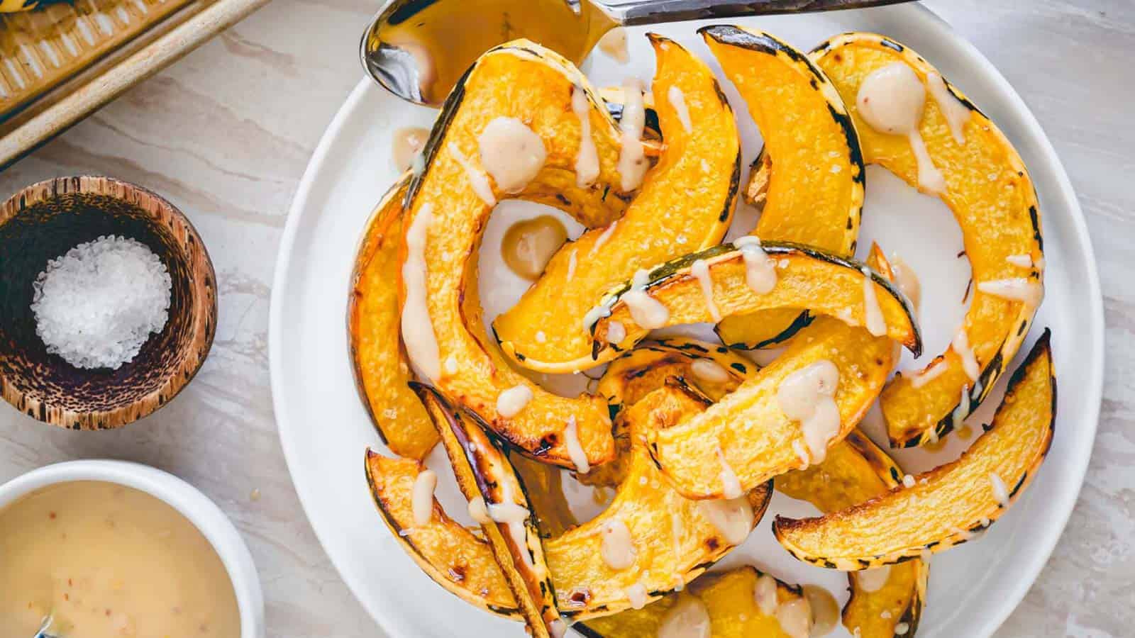 A plate of roasted sweet dumpling squash with a maple tahini sauce drizzled on top.