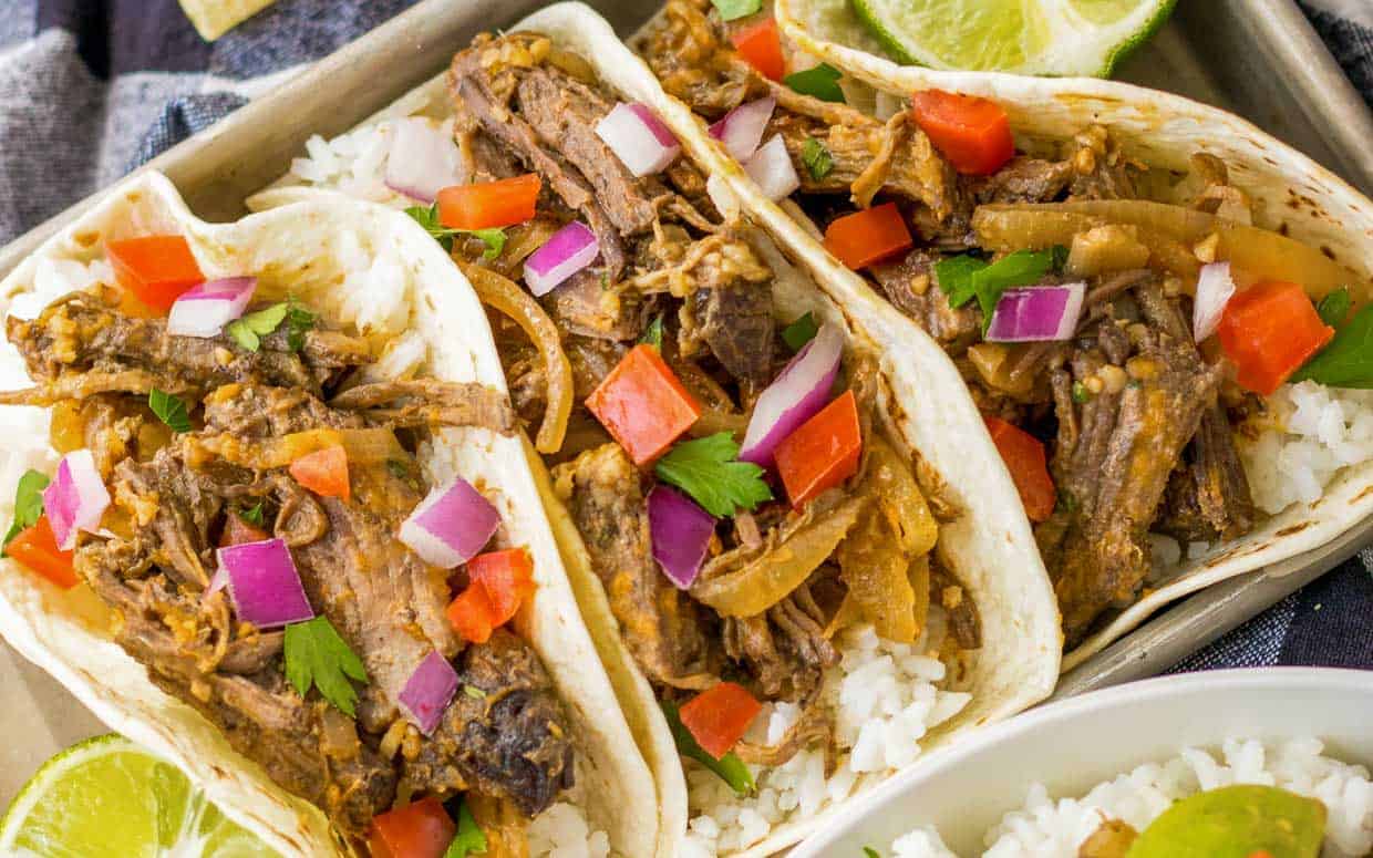 Barbacoa tacos on a tray topped with peppers and onions.