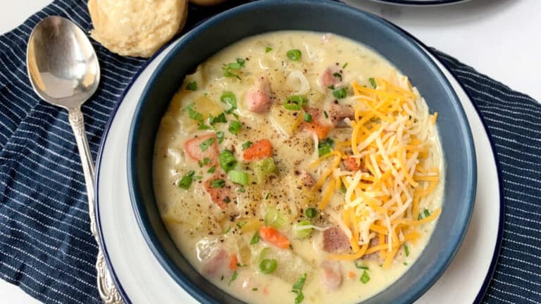 A bowl of soup with cheese and biscuits on a table.