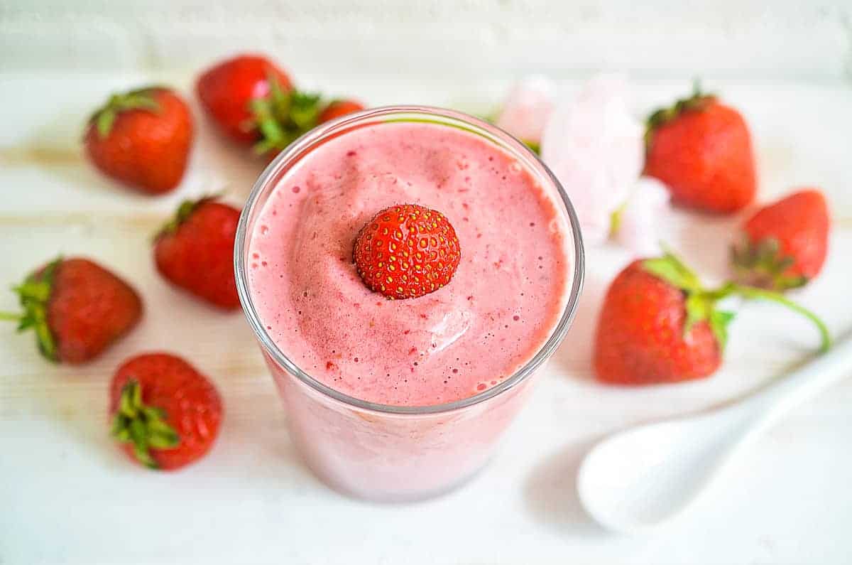 An easy breakfast strawberry smoothie in a glass surrounded by strawberries.