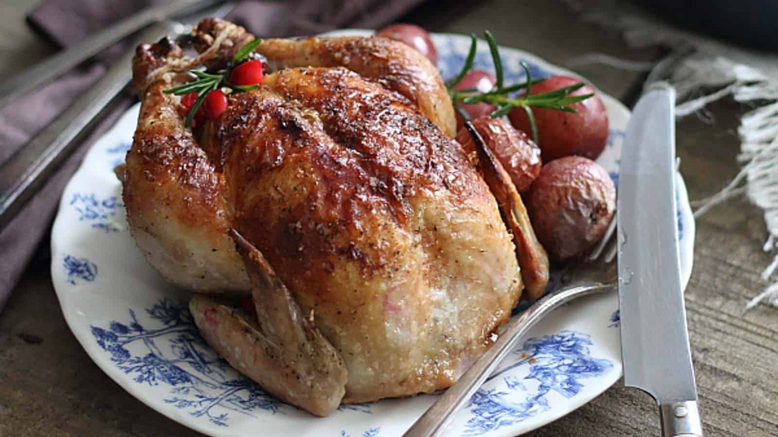 Roasted Cornish hens on a plate with potatoes and herbs.