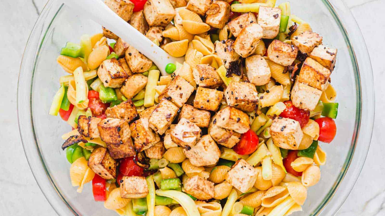 Tofu balsamic pasta salad in a glass bowl with white rubber spatula.