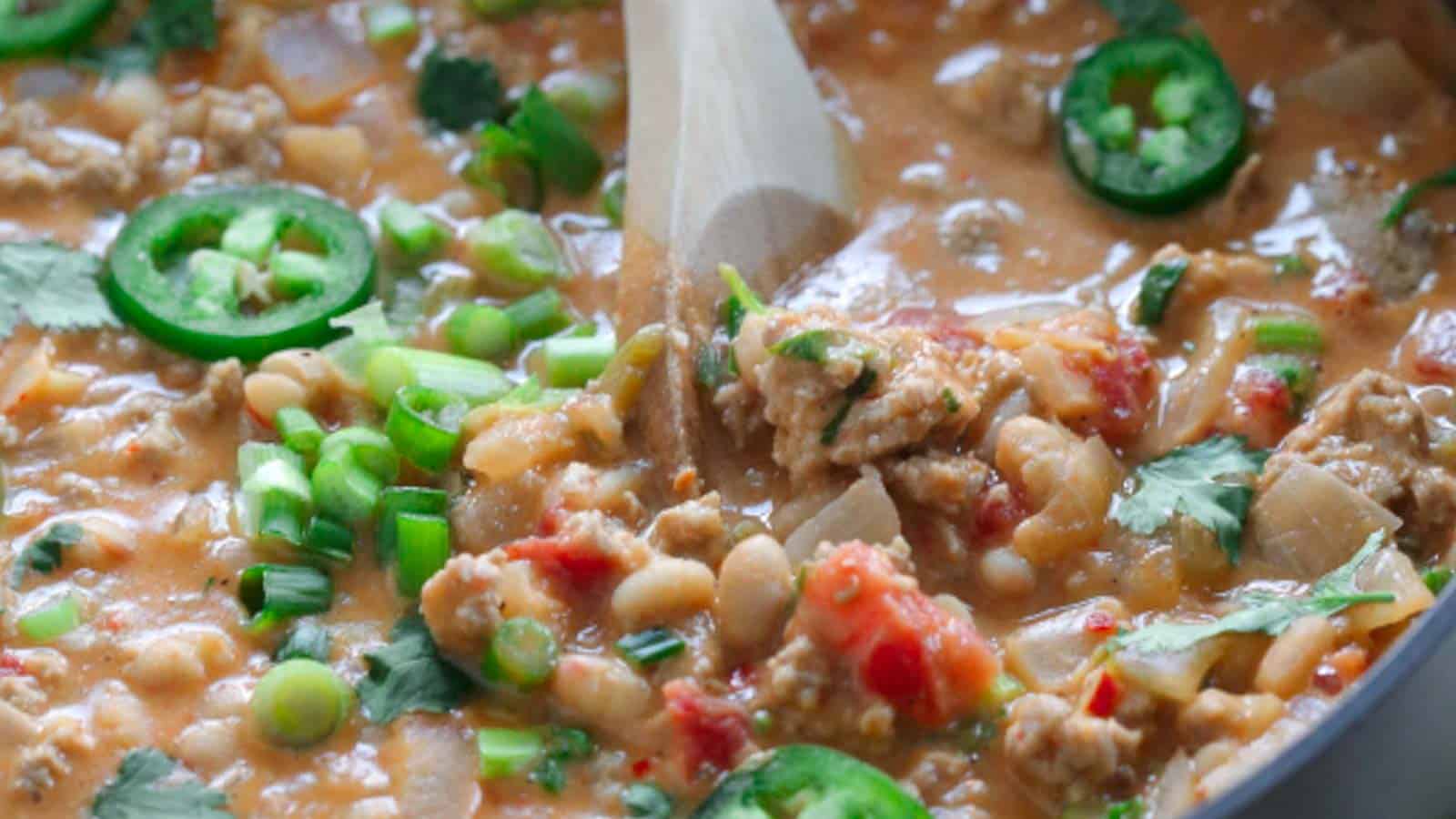 A skillet full of meat and beans in a pan with a wooden spoon.