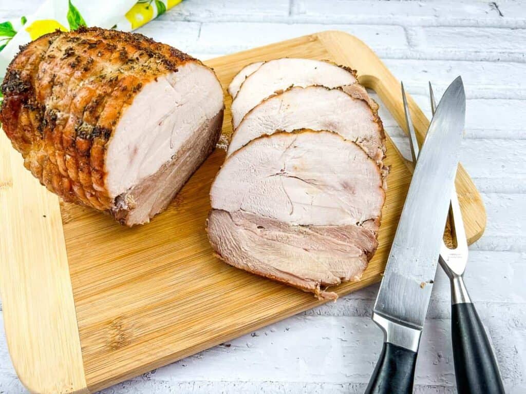 A piece of roasted turkey on a cutting board with a knife.