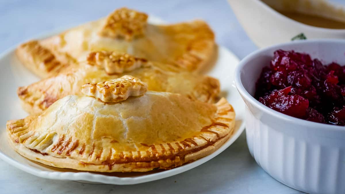 Turkey hand pies on a plate next to cranberry sauce.