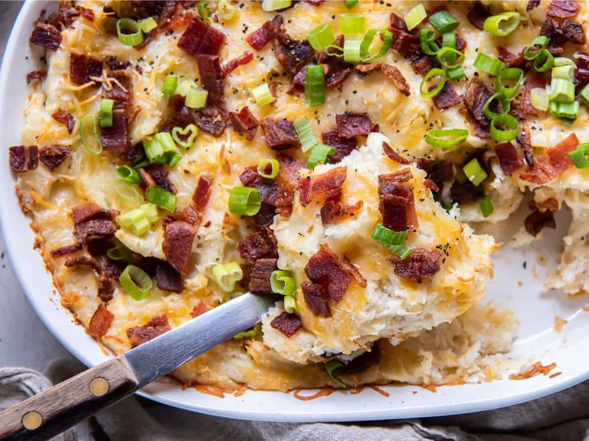 Closeup of twice baked mashed potatoes in a casserole dish with a serving spoon taking a scoop out.