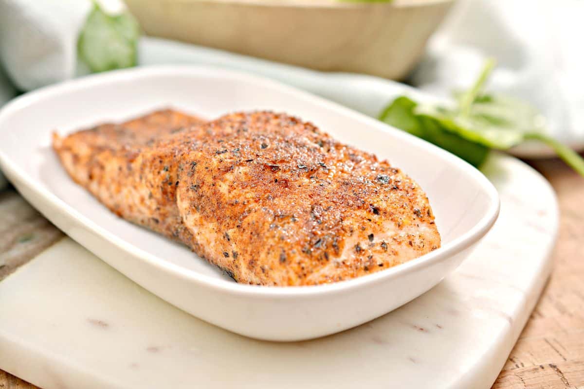 A piece of salmon is sitting on a white plate.