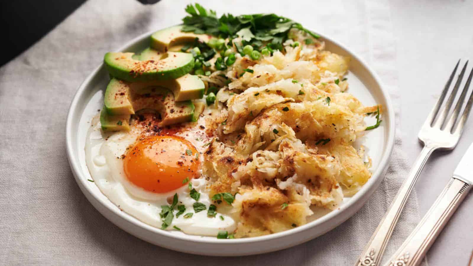 A plate with hash browns, eggs and avocado on a table.