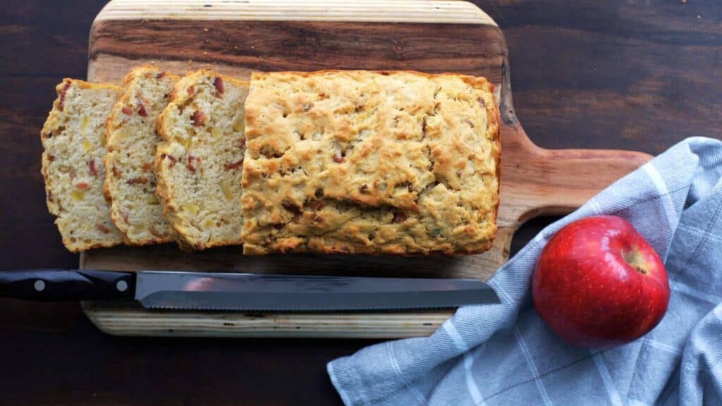 A slice of apple beer bread on a cutting board with a knife.