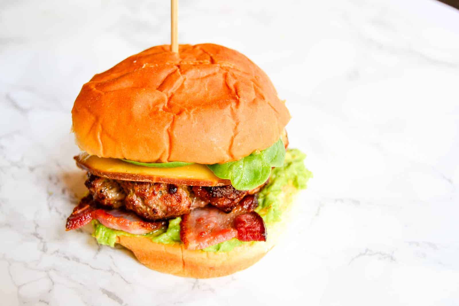 An up-close shot of bacon-avocado ground beef burger on a flat white surface.