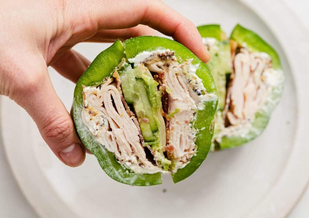 A person holding a stuffed pepper sandwich over a plate.