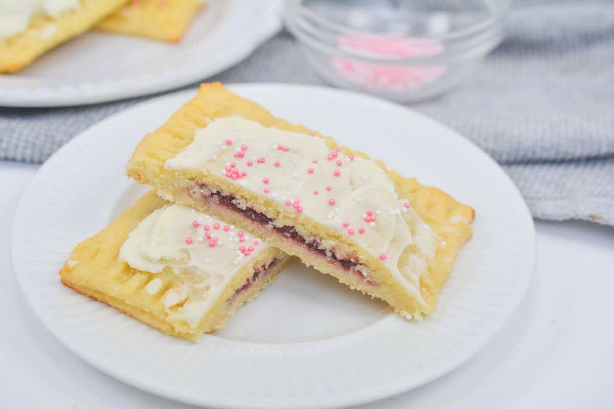 A plate with a slice of a cookie with frosting and sprinkles.