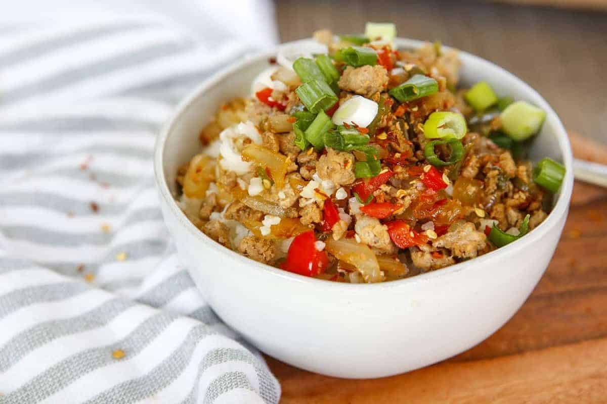 A bowl of cauliflower rice with meat and vegetables on a cutting board.