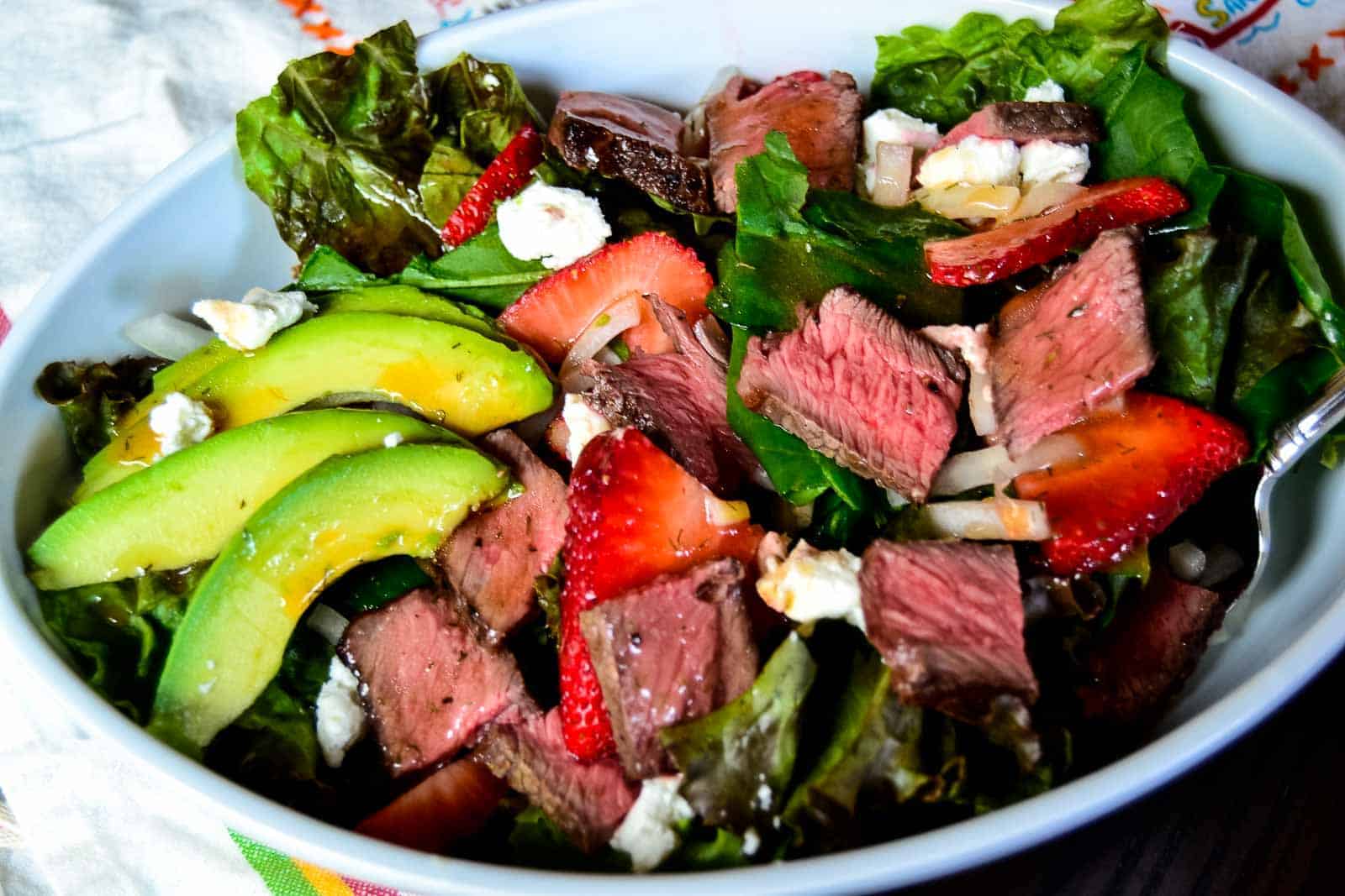 A bowl of winter salad with strawberries, avocado, and feta cheese.