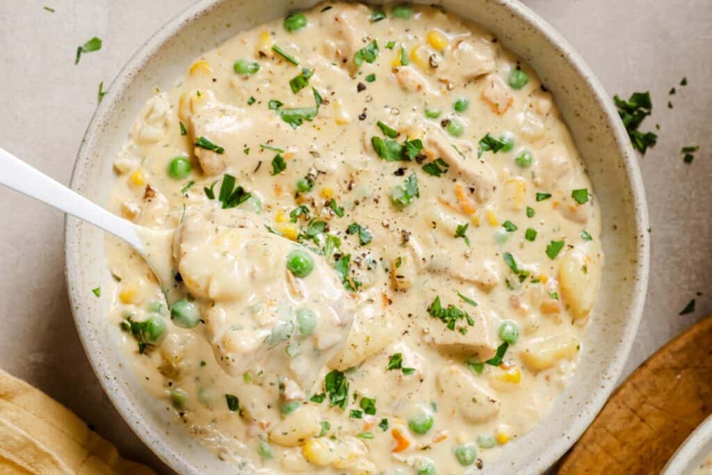 Chicken pot pie soup in a bowl with peas and carrots.