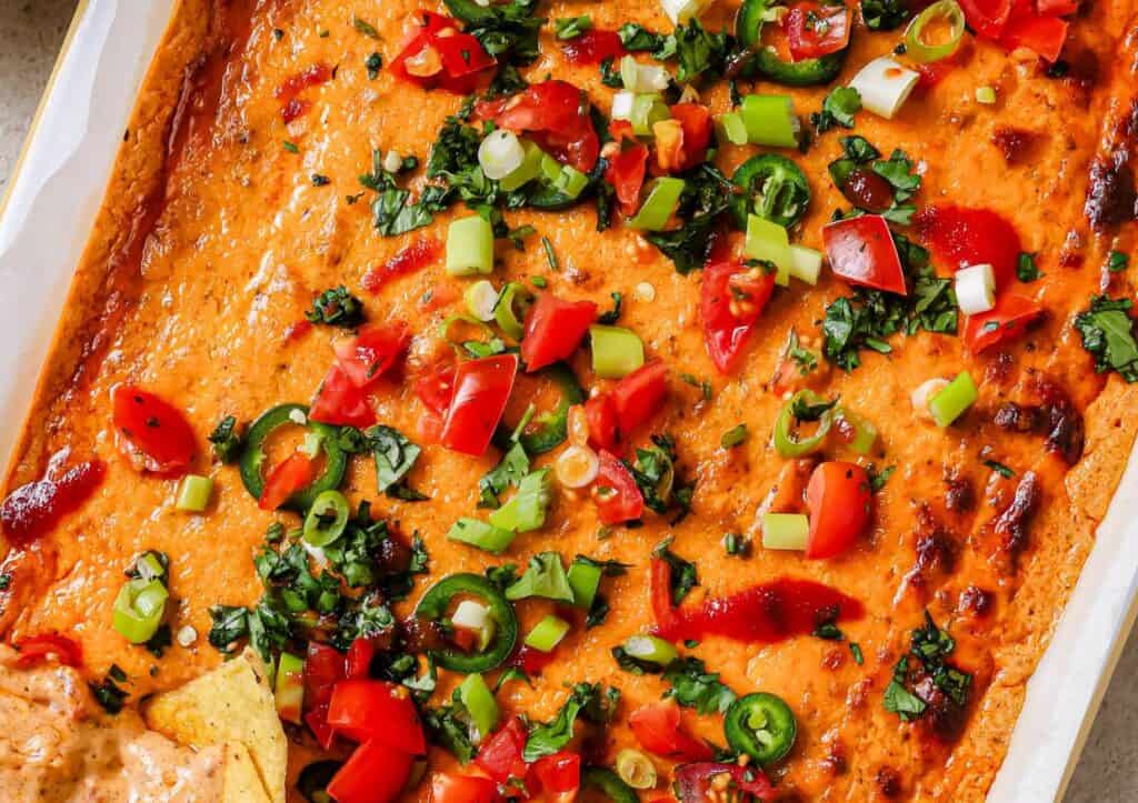 A white baking dish with chili cheese dip and tortilla chips.