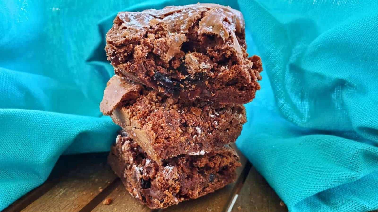 Image shows A stack of chocolate brownies on top of a blue cloth.