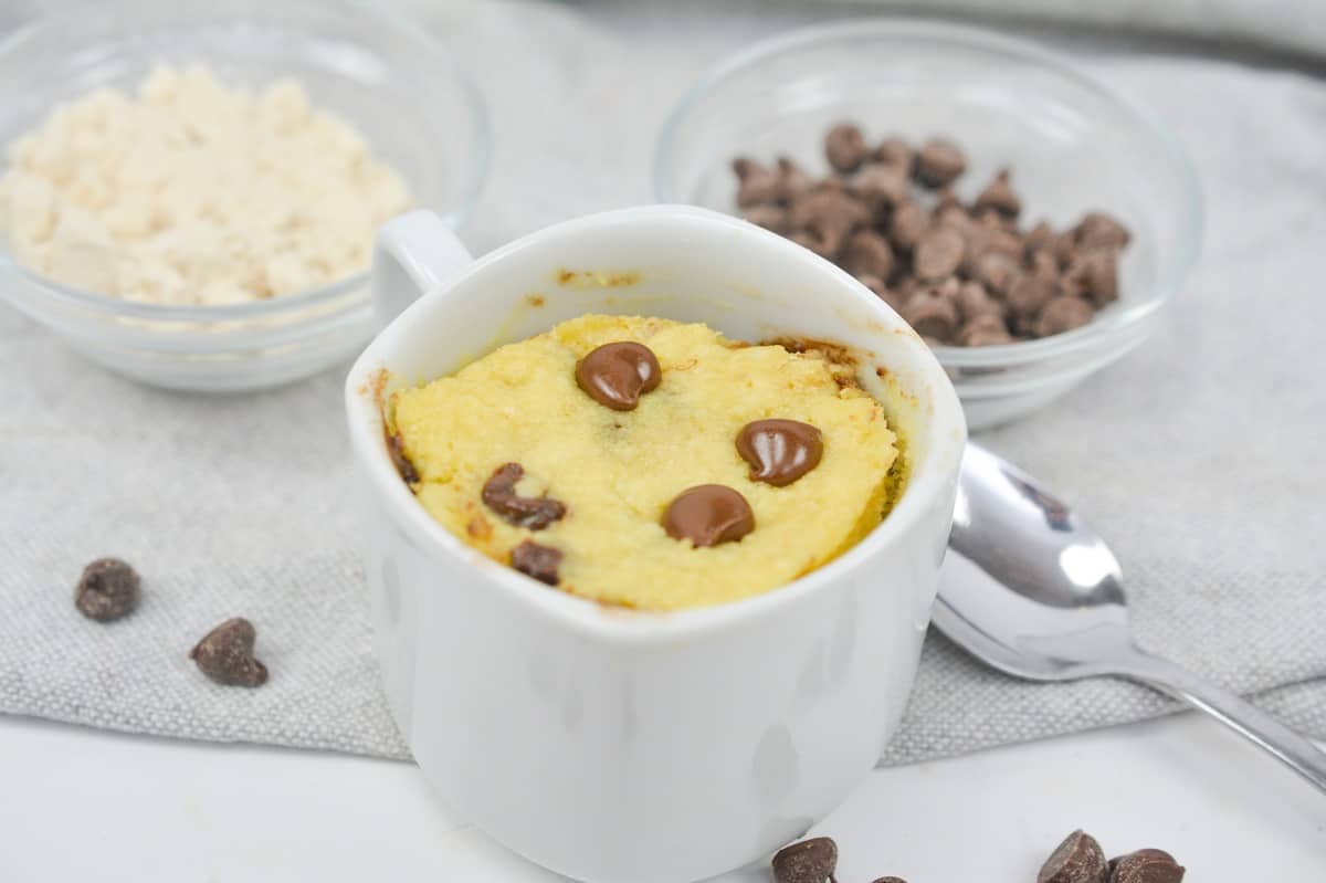 A mug with chocolate chips and a spoon next to it.