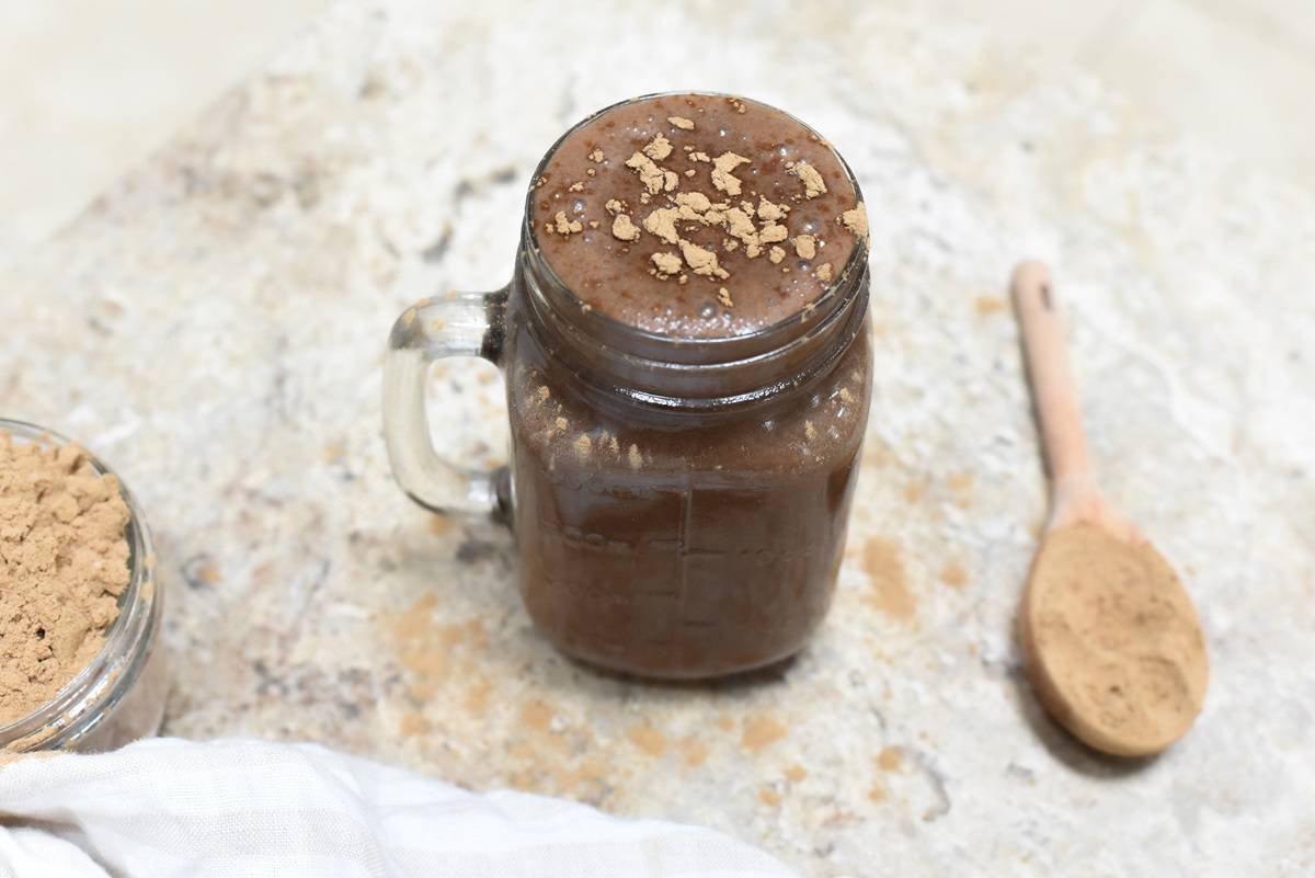 A chocolate smoothie in a jar with a spoon next to it.