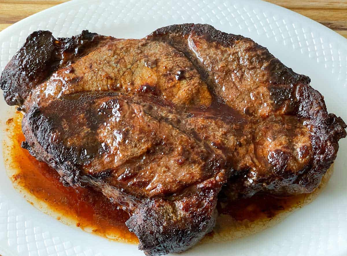 Chuck roast on a white platter with the juices. 