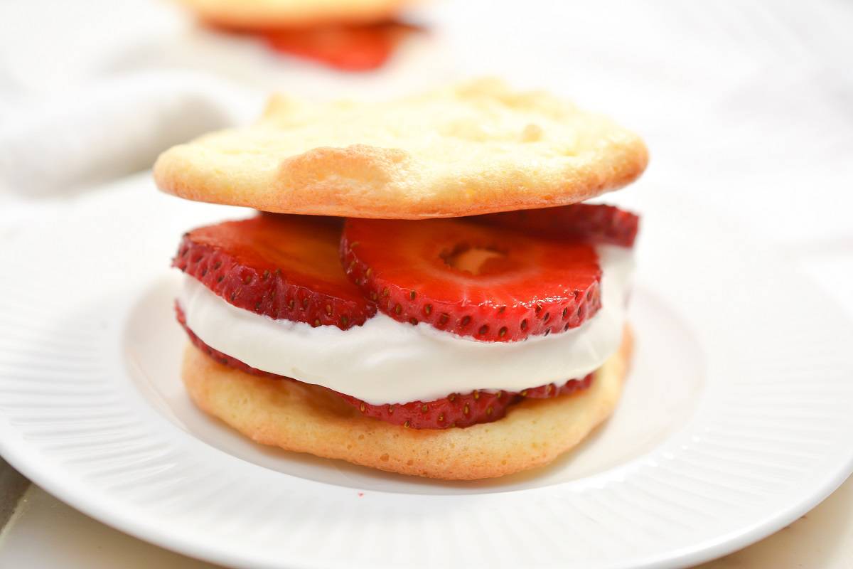 A sandwich with strawberries and cream on a white plate.