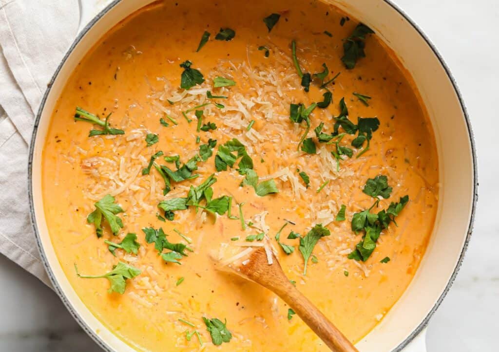 A pot of soup with parmesan cheese and parsley.