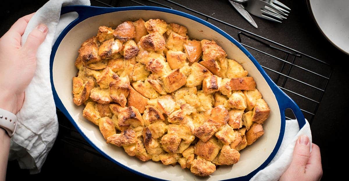 A person is holding a dish of bread pudding.