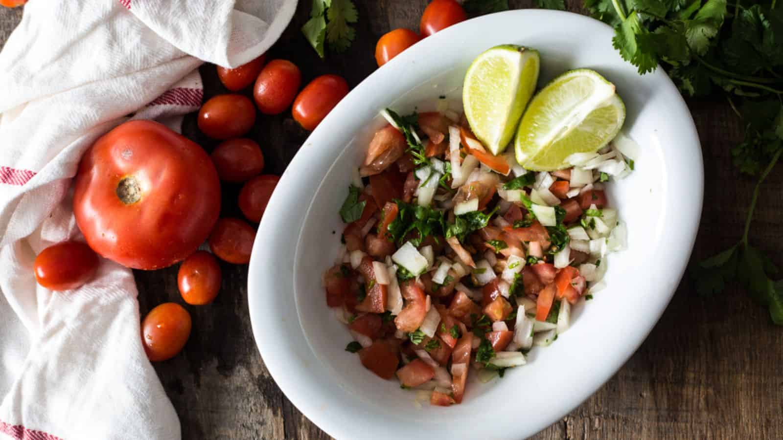 A bowl of salsa with tomatoes, onions and limes.