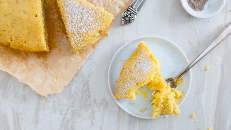 A slice of orange cake on a plate with a fork.