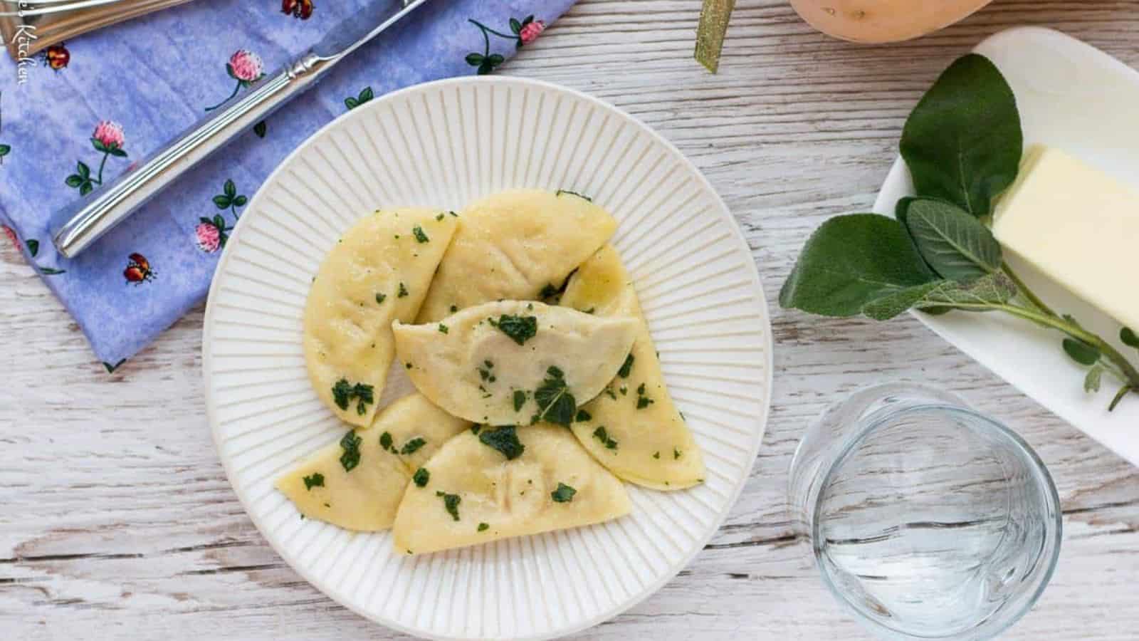 A plate of dumplings with herbs and butter on a wooden table.