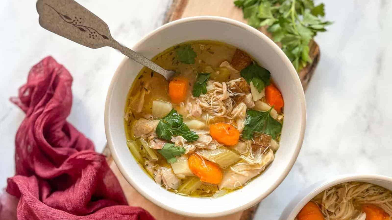 A white bowl of Instant Pot Chicken Stew sits on a rustic wooden cutting board with a red linen on a white marble counter.