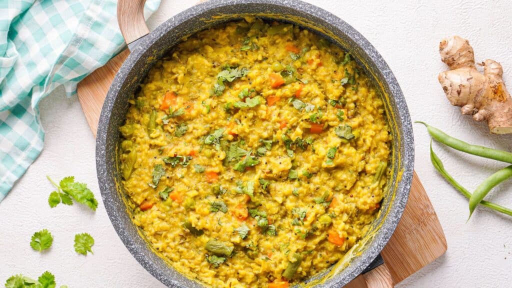 A pan with a bowl of Indian kitchari on a wooden cutting board.