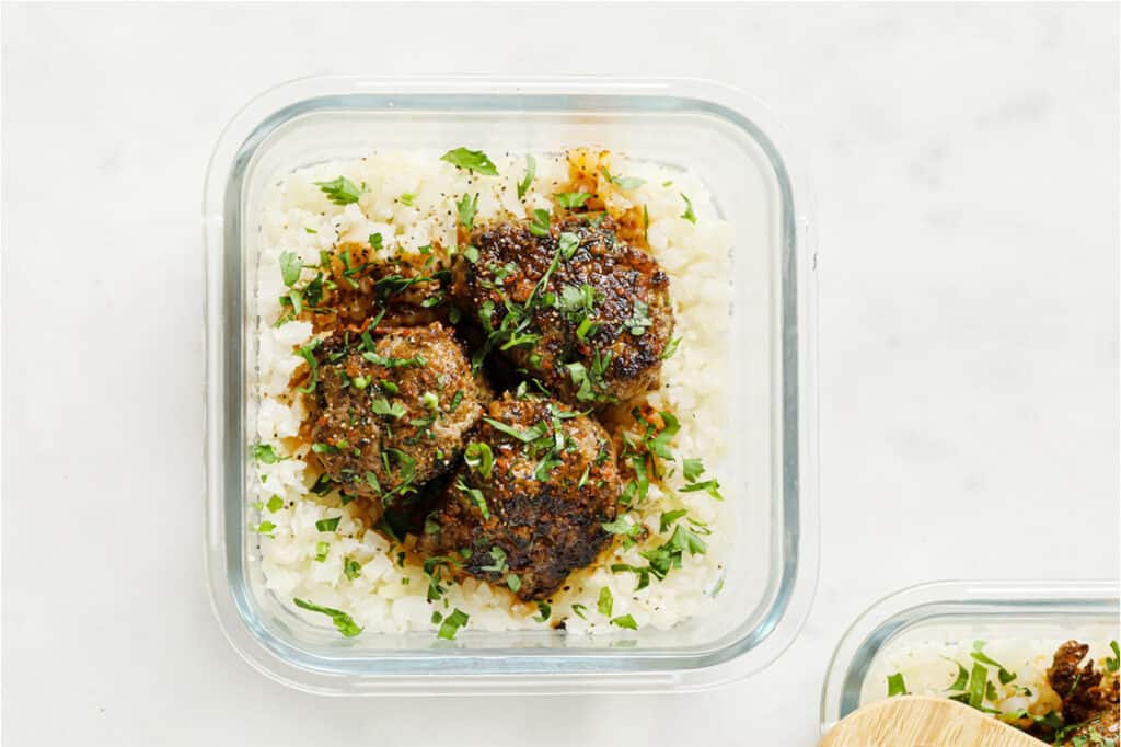 Two containers filled with cauliflower rice and meatballs.