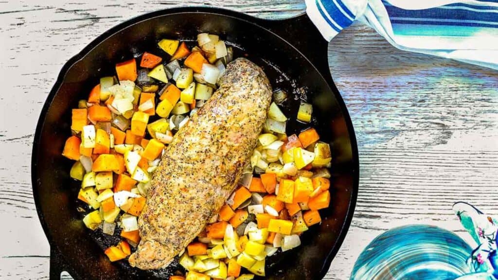 A cast iron skillet filled with pork tenderloin and vegetables.