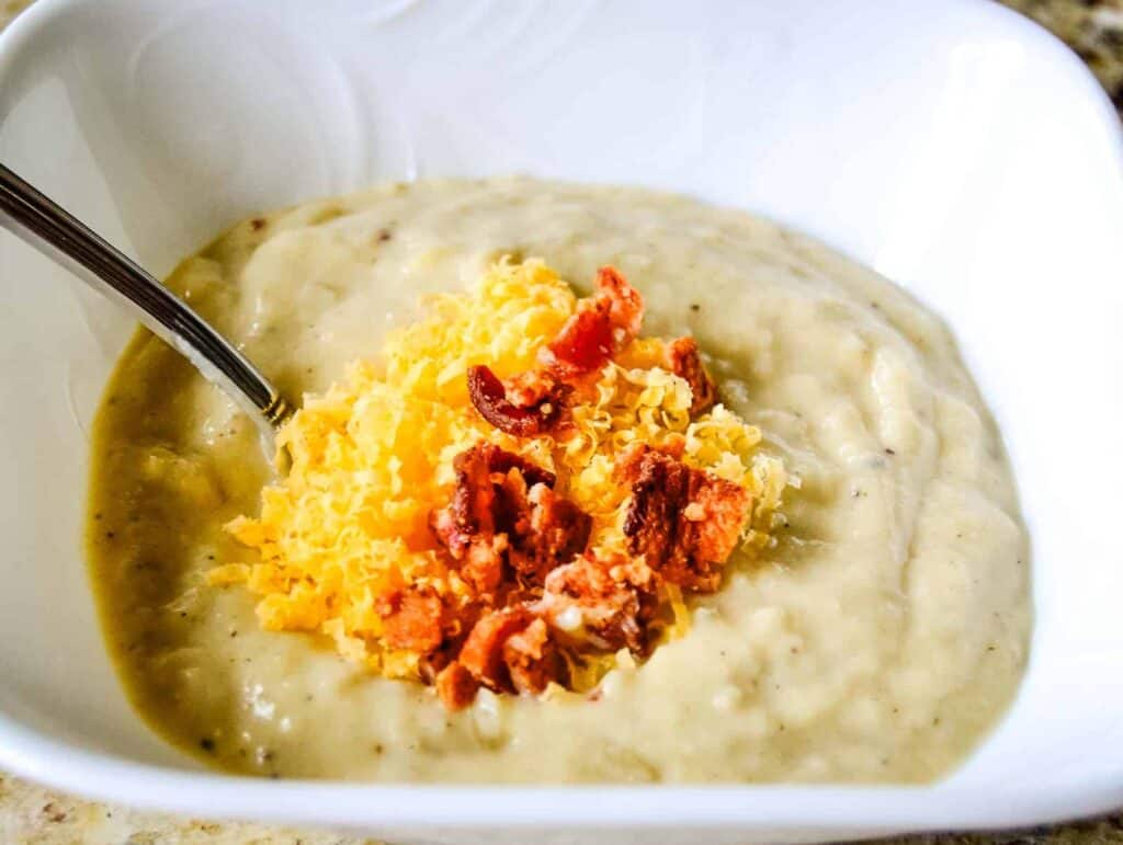 Cheesy mashed potatoes in a white bowl with a spoon, perfect for indulging in comfort food.