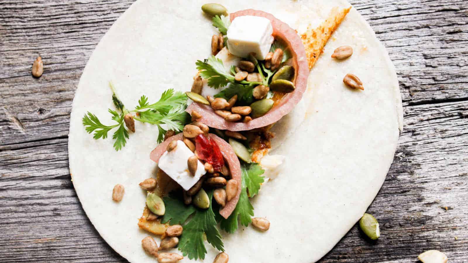 A burrito with feta, tomatoes and herbs on a wooden table.