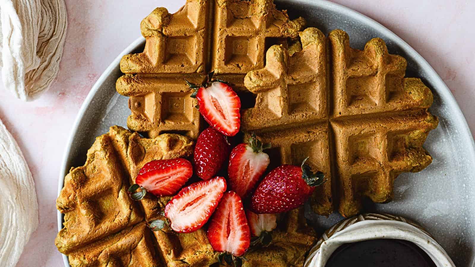 A plate of waffles with strawberries and syrup.