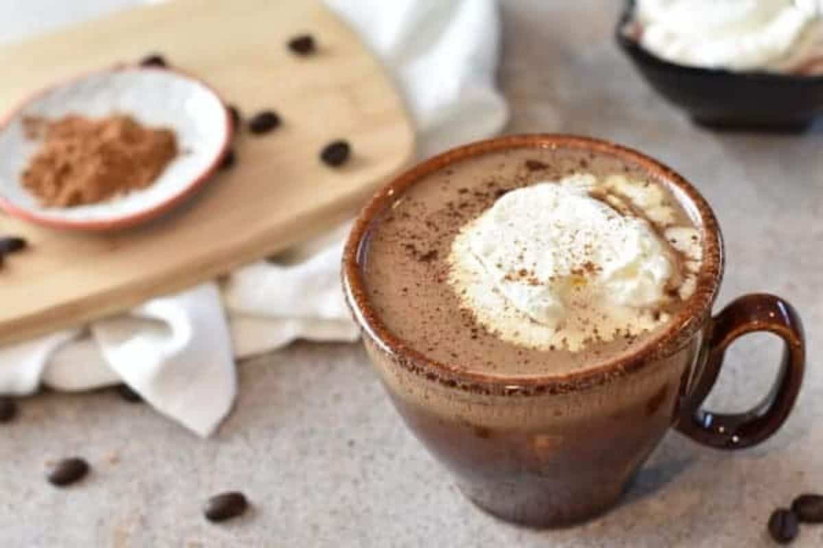 A cup of coffee with whipped cream and coffee beans.