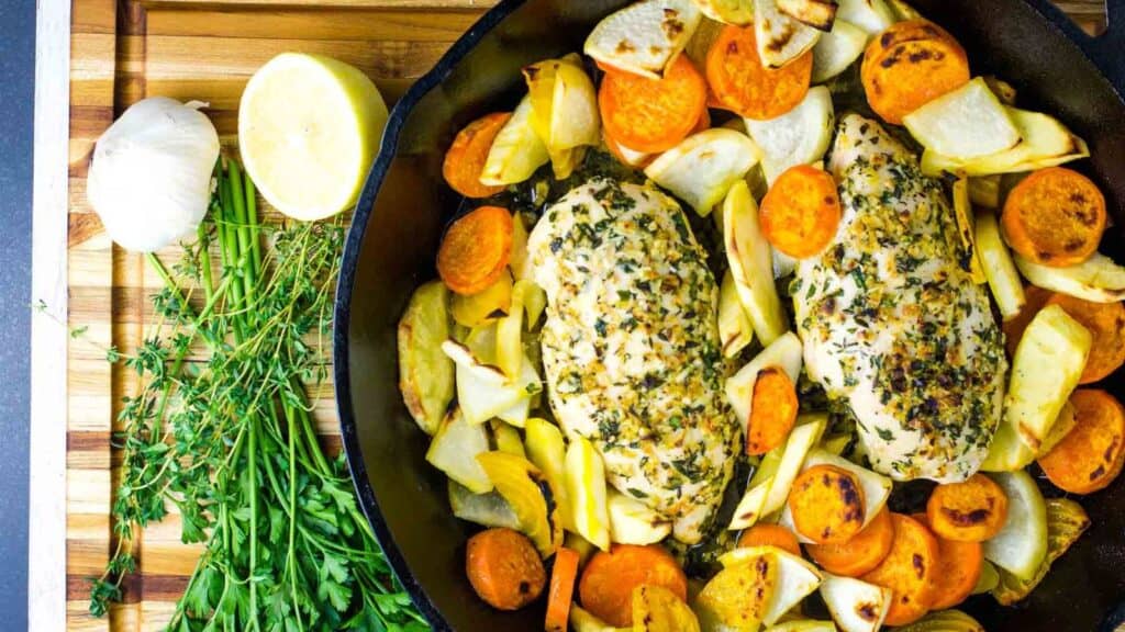 A skillet filled with chicken, carrots, parsnips, and herbs.