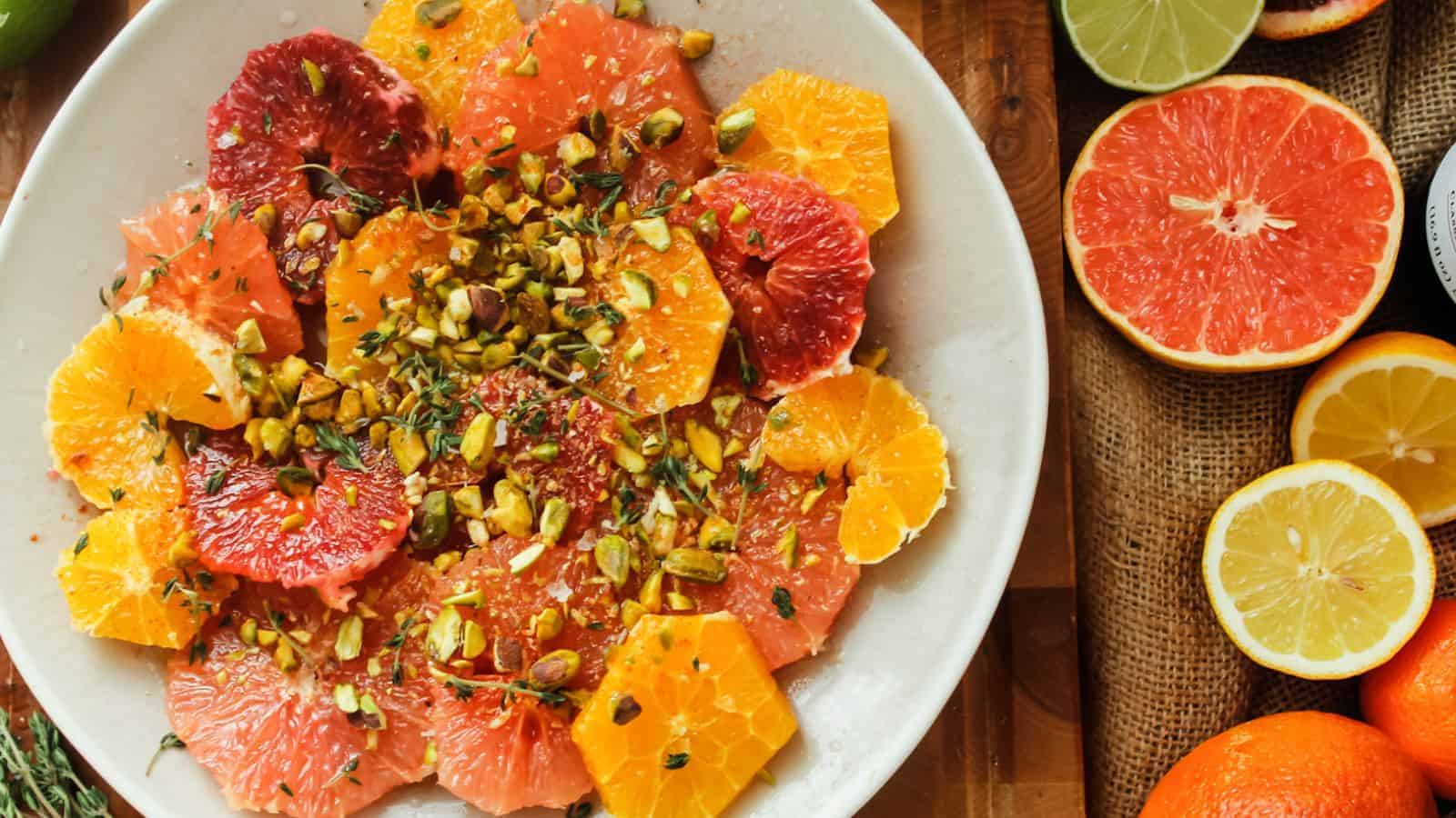 A plate of winter fruits, including oranges and grapefruits, accompanied by a handful of pistachios.