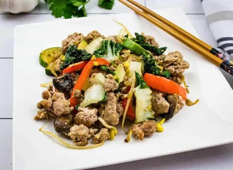 A white plate with meat, vegetables and chopsticks.