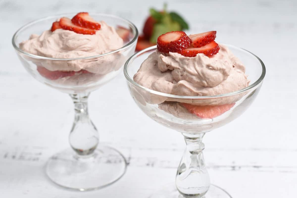 Two glasses with whipped cream and strawberries in them.