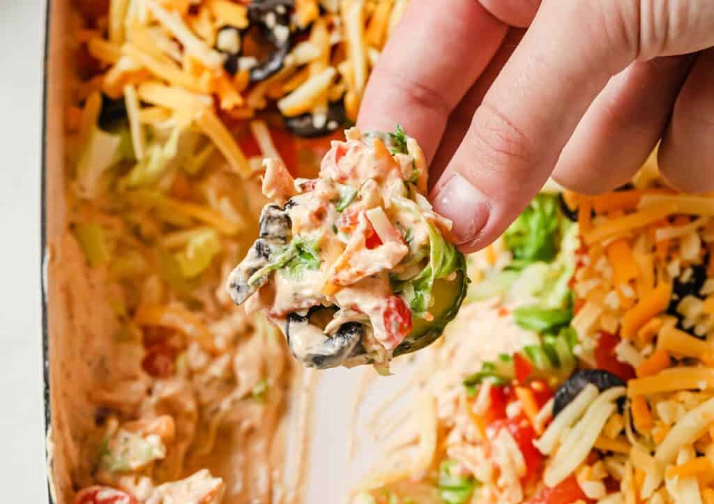 A hand holding a cucumber slice topped with taco dip.