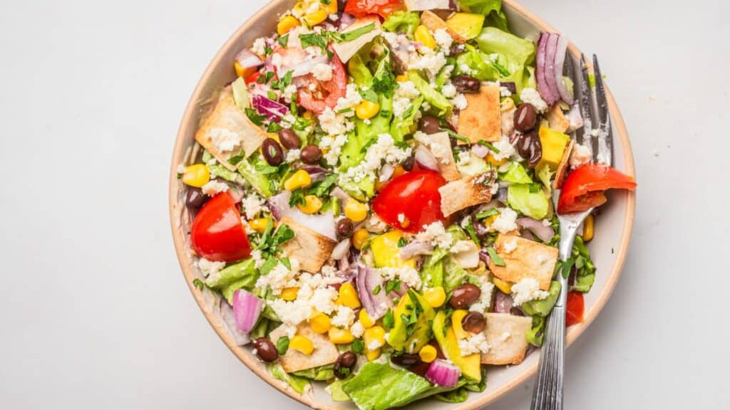 A bowl of taco salad with black beans, corn, tomatoes and beans.