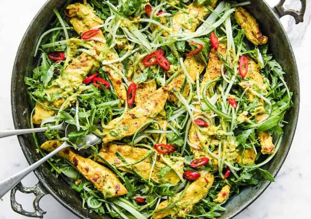 A bowl of chicken and arugula salad with two forks.